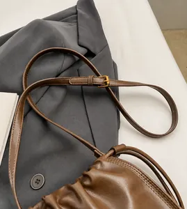 Detail of adjustable shoulder strap with golden metal buckle on brown leather bucket bag