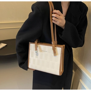 Detail of a minimalist beige tote bag with textured surface and brown leather handles