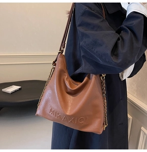 Dettaglio della borsa tote in pelle marrone con logo e tracolla a catena dorata