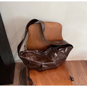 Detail of deep brown patent leather hobo bag with pleated texture on a vintage chair
