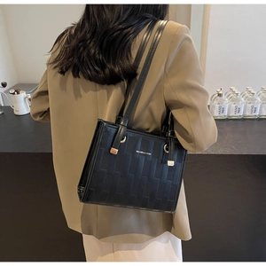Side view of black faux leather tote bag with geometric woven pattern and gold hardware
