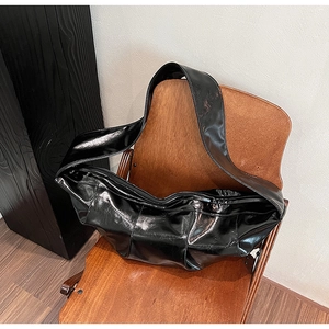 Detail of black glossy patent leather hobo bag with pleats on a vintage wooden chair