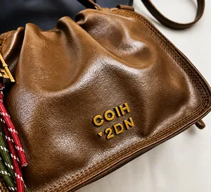 Detail view of brown leather bucket bag with metal letters and colorful woven cord