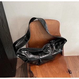 Detail of black glossy leather hobo bag with wide strap on a vintage wooden chair