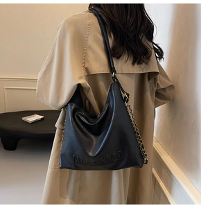 Dettaglio della borsa tote in pelle nera con logo in rilievo e catena decorativa dorata