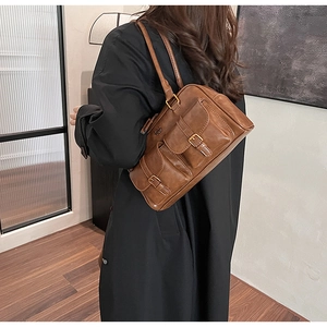 Detail of dark brown retro shoulder bag showing two front buckled pockets and metal logo