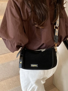 Black matte crescent crossbody bag with patterned wide strap worn by model on stairs