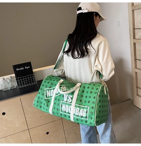 Dettaglio della grande borsa da viaggio verde con manici bianchi indossata da una modella