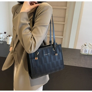 Close-up of black quilted tote bag with gold metal logo and fine stitching details