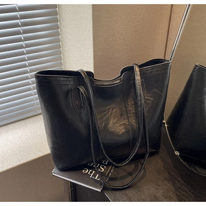 Close-up of a large black tote bag with vintage glossy texture and a secure top zipper