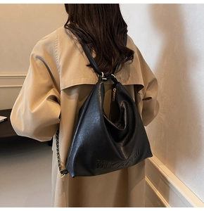 Modella che indossa una grande borsa tote in pelle nera con dettagli dorati e cappotto beige