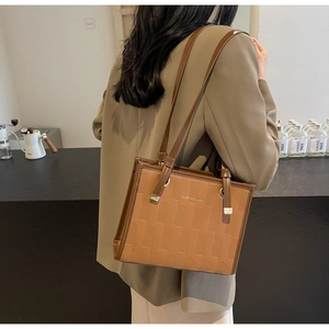 Detail of tan tote bag featuring intricate woven texture and golden metallic buckles