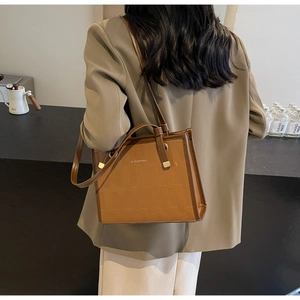 Detail of caramel brown tote bag showing woven texture and golden metal eyelets on strap