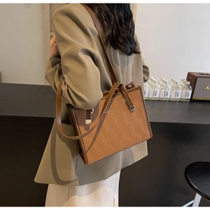 Detailed macro view of brown textured tote bag featuring geometric embossed leather and gold rings