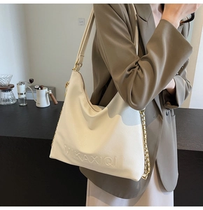 Dettaglio della borsa tote crema con scritta a rilievo e tracolla in catena metallica