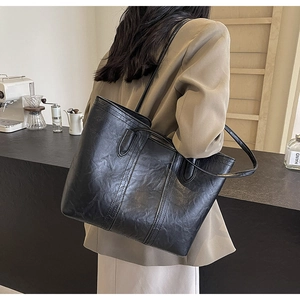 Side view of large black leather tote bag worn by model in a cozy cafe setting