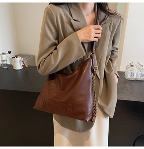 Dettaglio borsa tote in pelle marrone scuro con tracolla a catena dorata e logo impresso