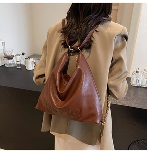 Dettaglio della borsa tote in pelle caramello con logo inciso e maglia a catena dorata