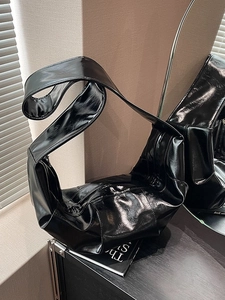 Modern black glossy crescent shoulder bag with wide strap in a minimalist setting