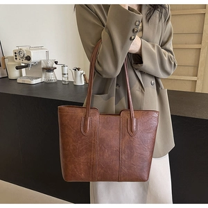 Brown faux leather tote bag with vertical stitching shown in a stylish cafe setting