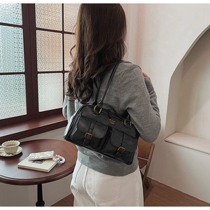 Detailed view of black matte leather shoulder bag with front buckle pockets and brand logo