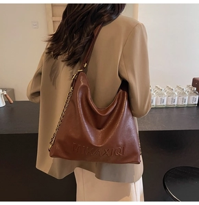Dettaglio della borsa tote in pelle marrone scuro con catena e logo in rilievo