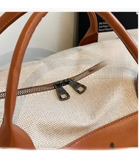 Close-up of smooth dual metal zippers on a beige canvas travel Boston bag with leather trim