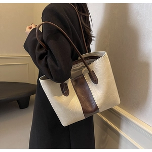 Detail view of large bi-color tote bag in cream and brown leather on model's shoulder