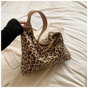 Close-up of leopard print tote bag with brown leather handles and pearl charm detail