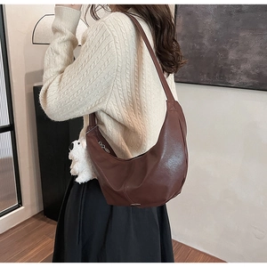 Detail view of a dark brown crescent leather crossbody bag with a plush bear charm