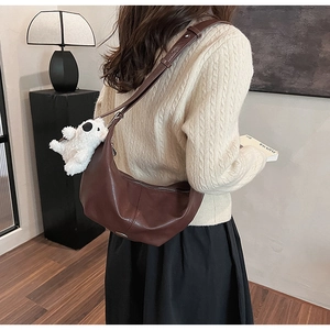 Detail of a brown leather hobo bag with a plush dog charm worn by a model