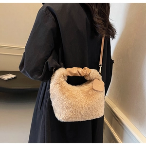 Detail of plush beige handbag featuring heart tag and golden chain strap on black coat