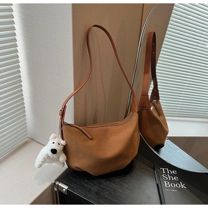 Detail of matte brown hobo bag with white puppy plush pendant and textured leather