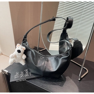 Detailed view of black matte leather hobo bag with white plush charm on a wooden surface