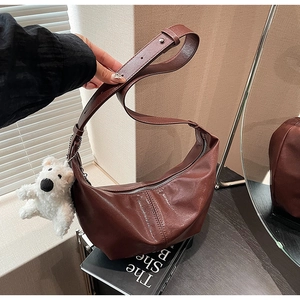 Detail of dark brown leather crescent bag with glossy texture and plush bear pendant