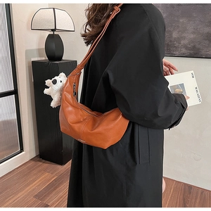 Detailed shot of brown crescent hobo bag with a white plush dog charm on a model