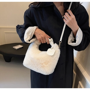 Close-up of white plush handbag with pleated handle and thin crossbody strap on black coat