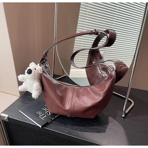 Close-up of vintage brown leather crescent bag with cute white puppy plush charm
