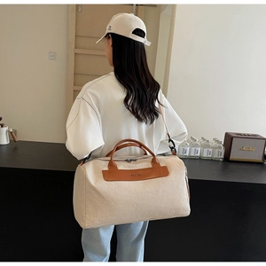 Detail of cream canvas travel bag showing brown leather logo patch and metal hardware hooks
