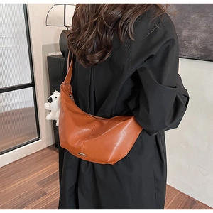 Detail of brown leather crescent bag featuring a metal buckle and plush puppy charm