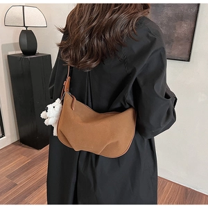 Side view of dark brown suede hobo bag with a plush white dog charm and pleated texture