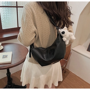 Detail of black matte leather crescent bag with plush puppy charm and wide strap