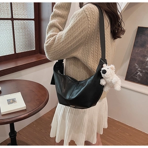 Detail of black semi-circle PU leather bag featuring a cute white puppy pendant accessory