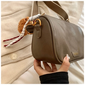 Detail of dark brown Boston bag with wide fabric strap and cute bear plush charm