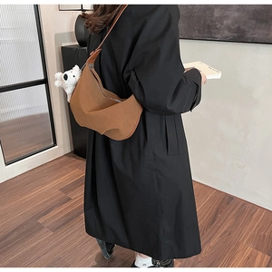 Brown frosted crescent crossbody bag with plush dog charm shown on a black coat