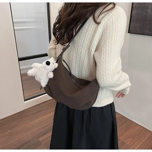 Detail of a brown matte hobo bag with a plush bear charm on a knit sweater backdrop