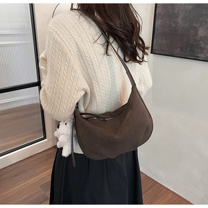 Close-up of deep brown suede crossbody bag with a cute white plush puppy pendant