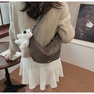 Detail of dark brown leather crescent bag with cute white puppy pendant and adjustable strap