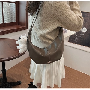 Detail of dark brown leather crescent bag with white plush charm in a warm indoor setting