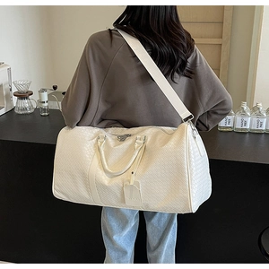 Dettaglio borsa da viaggio bianca intrecciata con manici superiori e tracolla regolabile